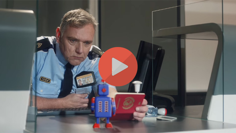 Spot publicitaire façon Michel Gondry : douanier examinant un jouet robot et un passeport au poste-frontière