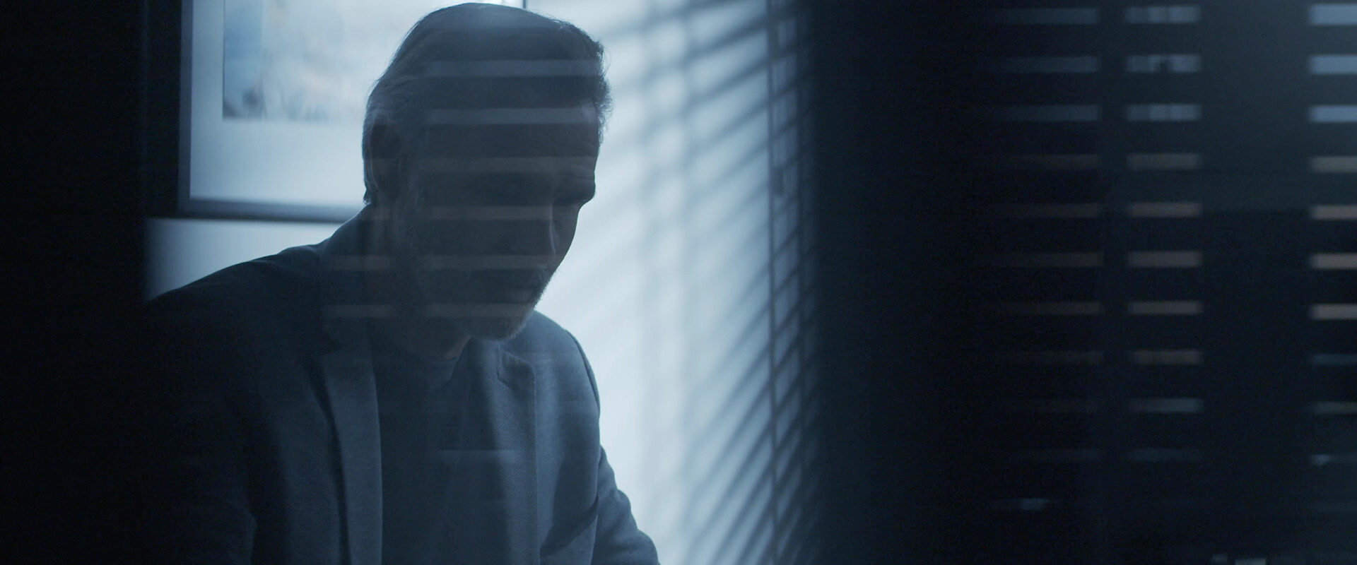 Film institutionnel Optimum Automotive : homme en costume dans un bureau à l'ambiance sombre et lumière de store