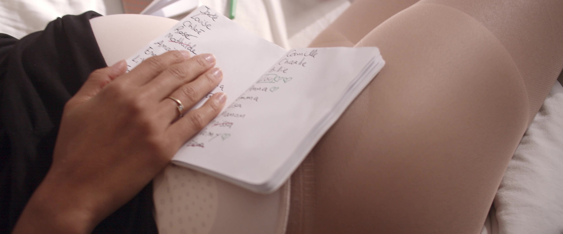 Tournage du film institutionnel Sigvaris : main sur un carnet de prénoms posé sur le ventre d'une femme enceinte