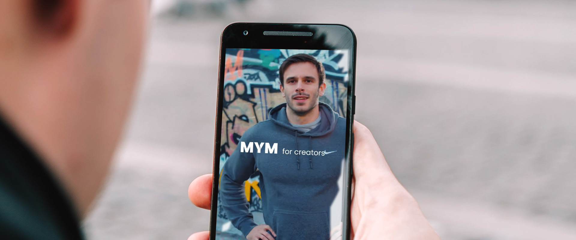 Spot publicitaire MYM for creators visionné sur smartphone, homme en sweat filmé devant un mur graffiti