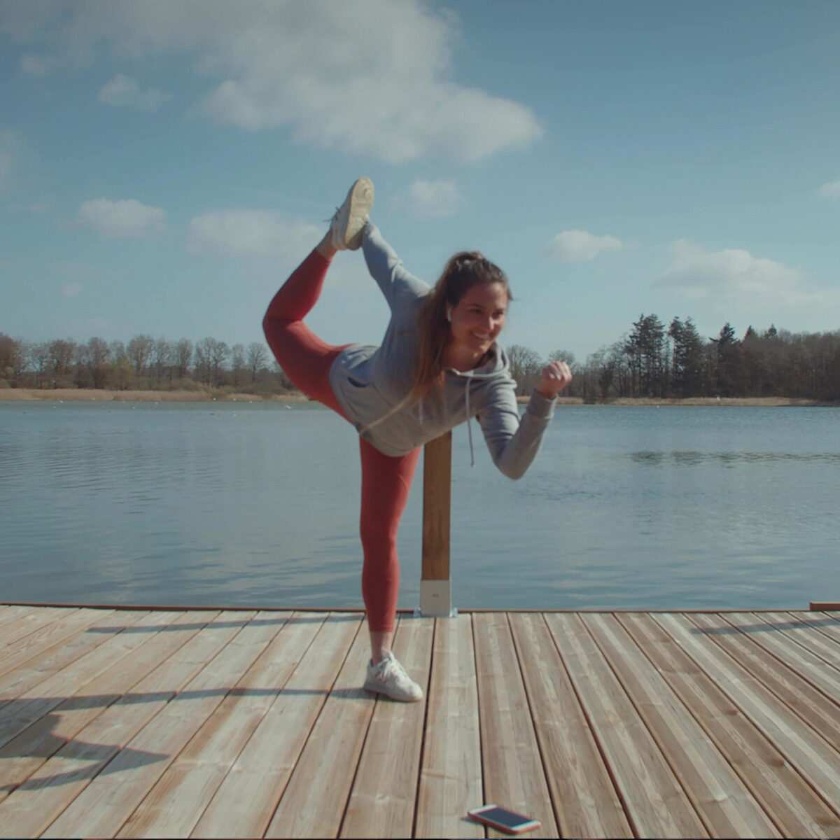 Spot publicitaire MYM : jeune femme en posture de yoga sur un ponton au bord d'un lac