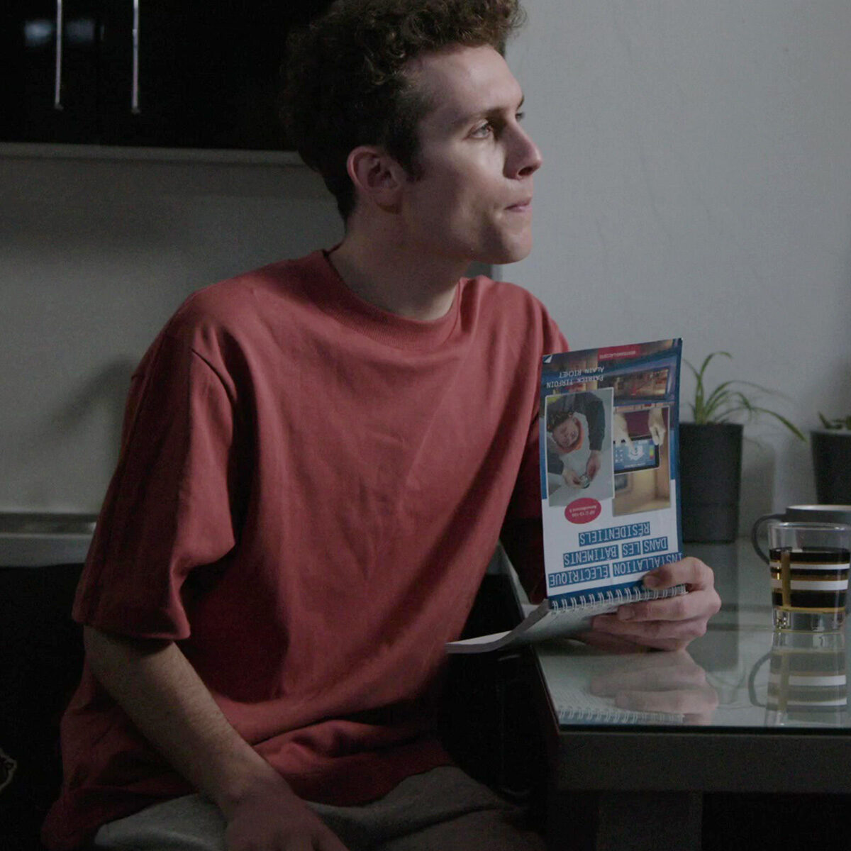 Spot publicitaire Nexans : jeune homme assis à table lisant une brochure sur l'installation électrique résidentielle