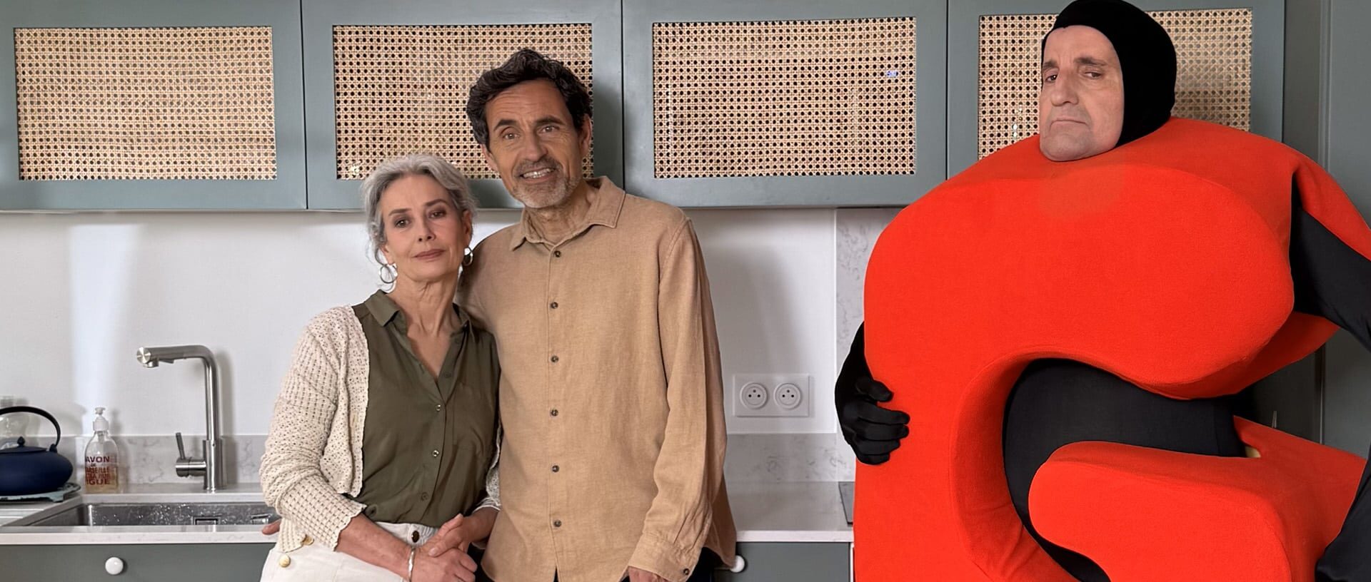 Tournage du spot publicitaire Bail Rénov' : couple en cuisine posant avec un mascotte costumée orange