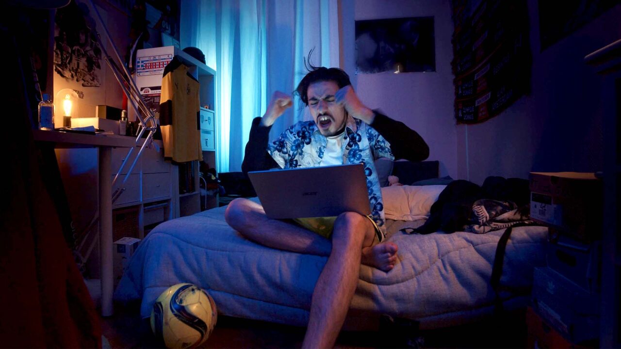 Jeune homme exultant sur son lit devant un laptop, lumière bleue — film publicitaire Mym, réseau social privé