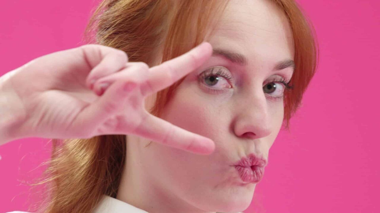 Comédienne rousse faisant un signe de main sur fond rose vif, film publicitaire Carestream Dental CS7200, imagerie dentaire