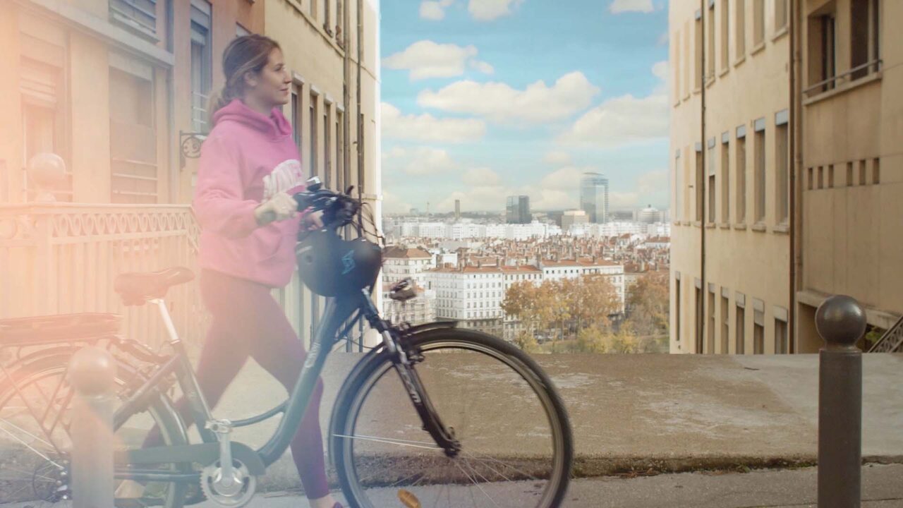 Jeune femme poussant un vélo électrique dans Lyon, campagne vidéo Feu Vert E-Roll 80, enseigne de distribution