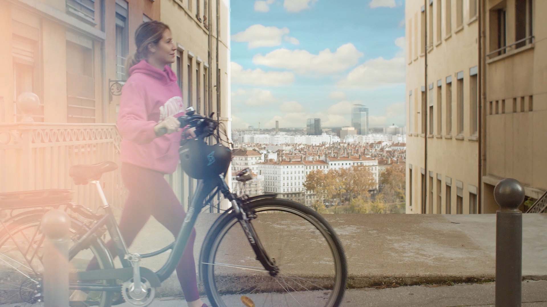 Jeune femme poussant un vélo électrique dans Lyon, campagne vidéo Feu Vert E-Roll 80, enseigne de distribution