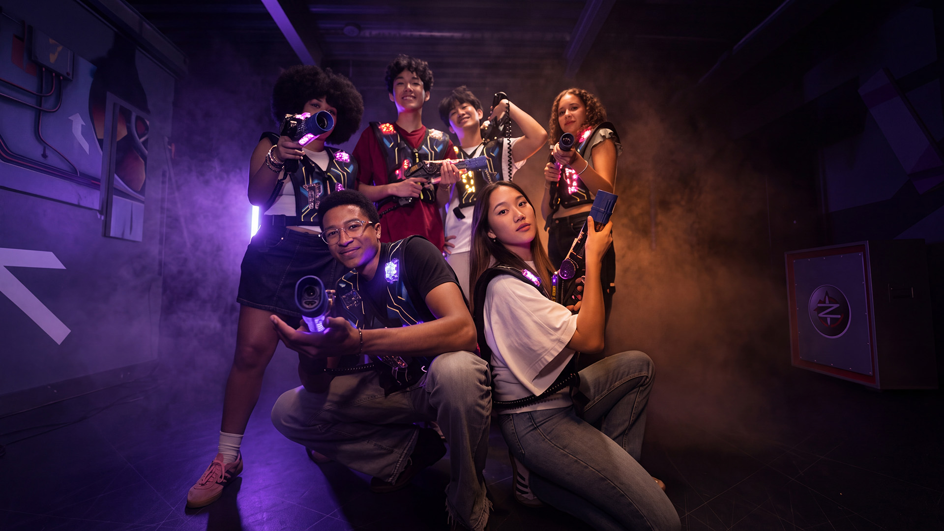 Spot publicitaire Megazone : six joueurs posent avec leurs lasers dans une arène enfumée aux néons violets