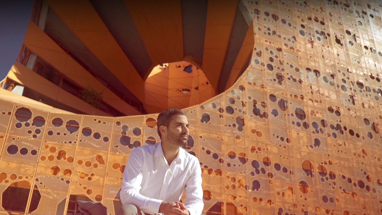 Dirigeant en chemise blanche devant une façade dorée ajourée, film d'entreprise Nexenture, services B2B