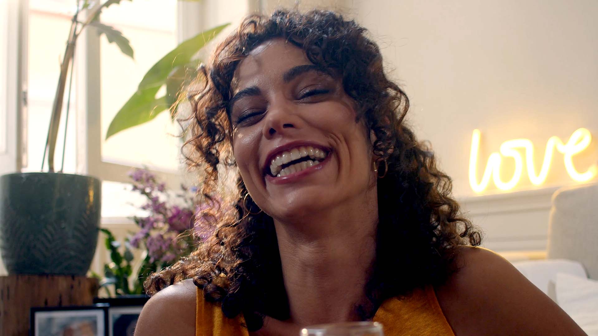 Femme aux cheveux bouclés riant dans un intérieur lumineux, spot publicitaire Sigvaris Maternité, compression médicale textile