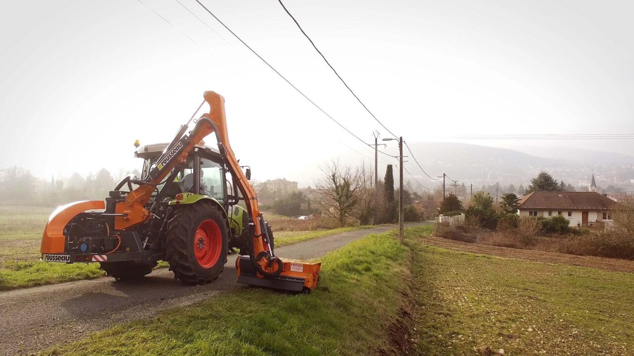 Tracteur Rousseau E-Kastor et bras de fauchage orange sur route rurale brumeuse, publicité vidéo