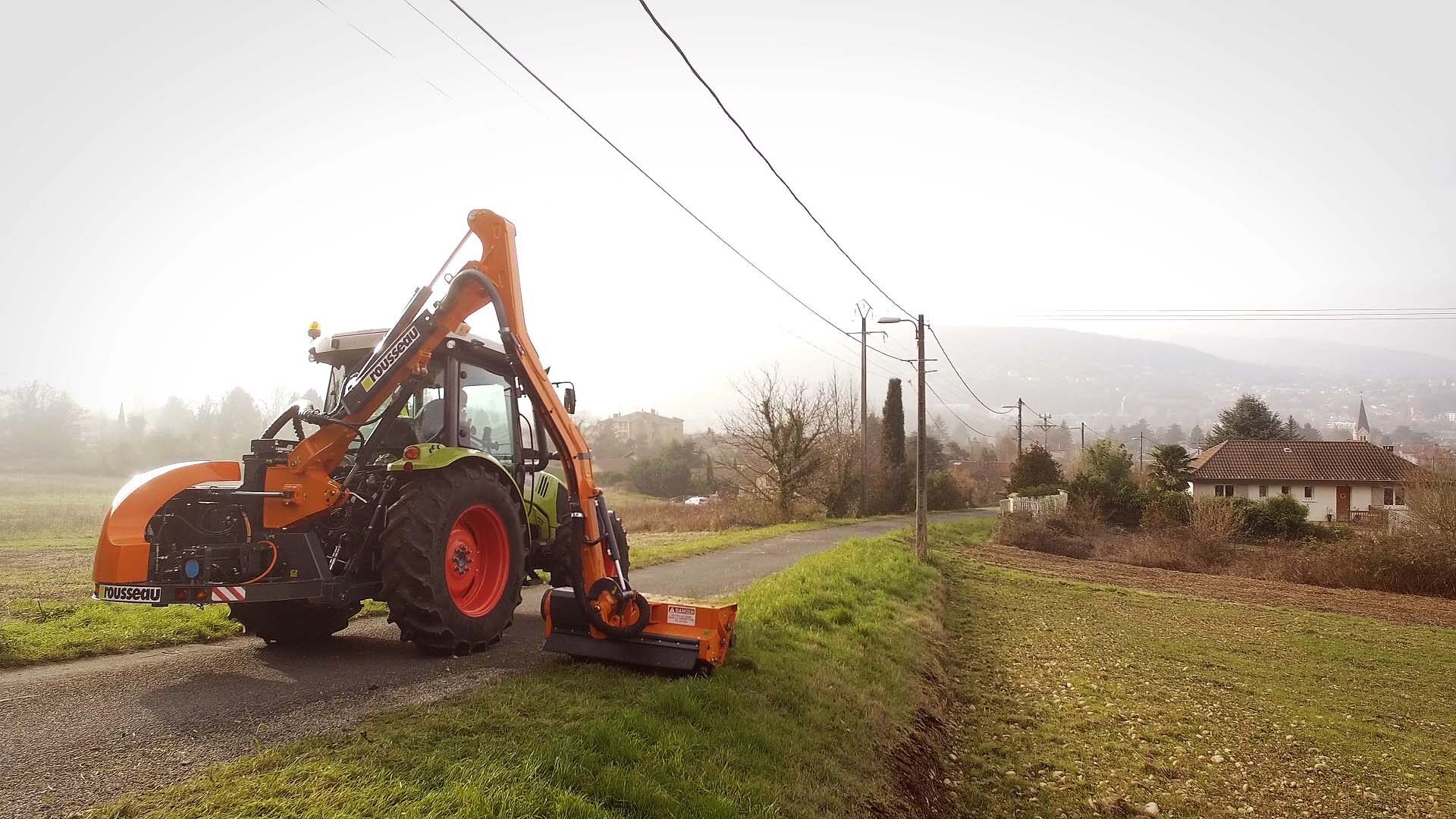 Tracteur Rousseau E-Kastor et bras de fauchage orange sur route rurale brumeuse, publicité vidéo