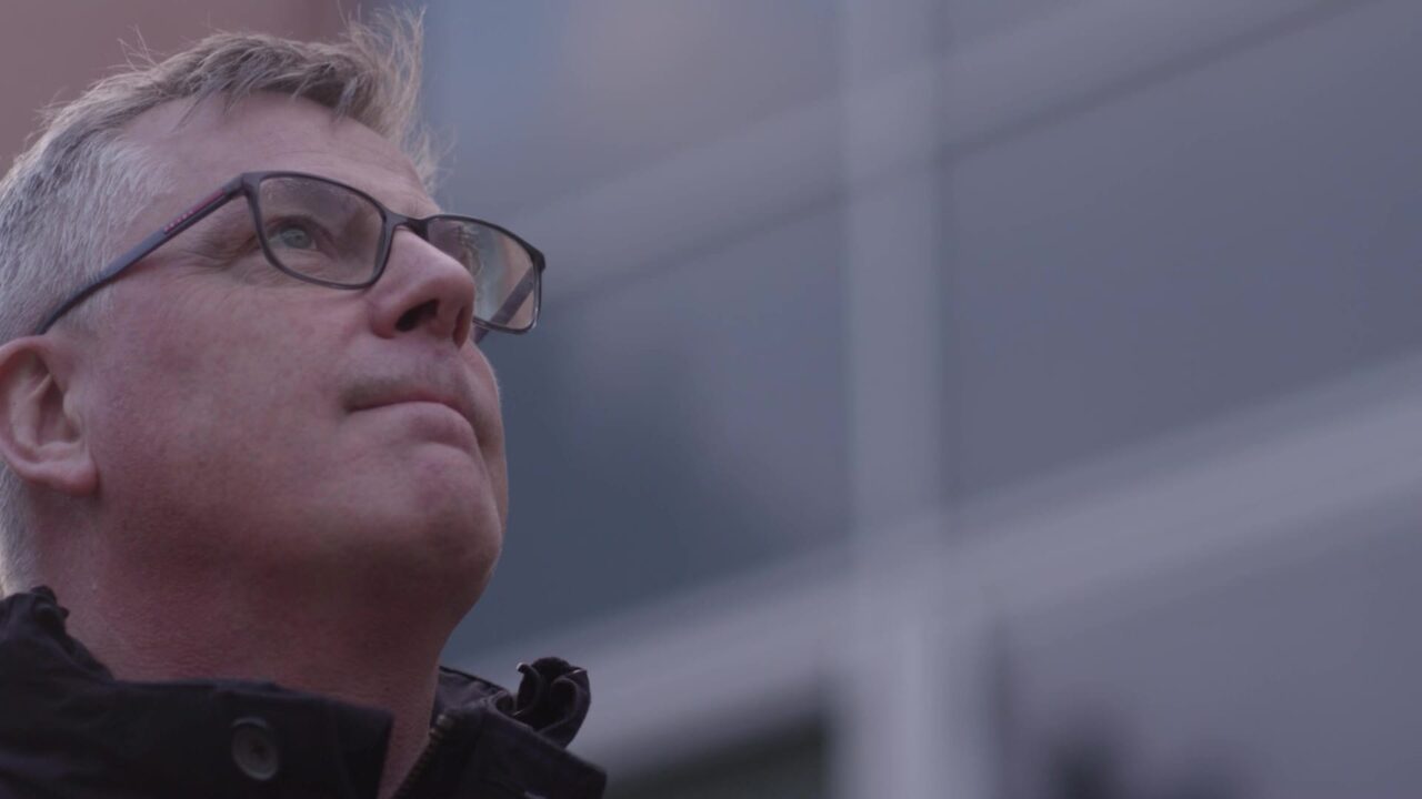 Alumni aux lunettes regardant vers le haut devant une façade vitrée, vidéo institutionnelle ESTP grande école de la construction