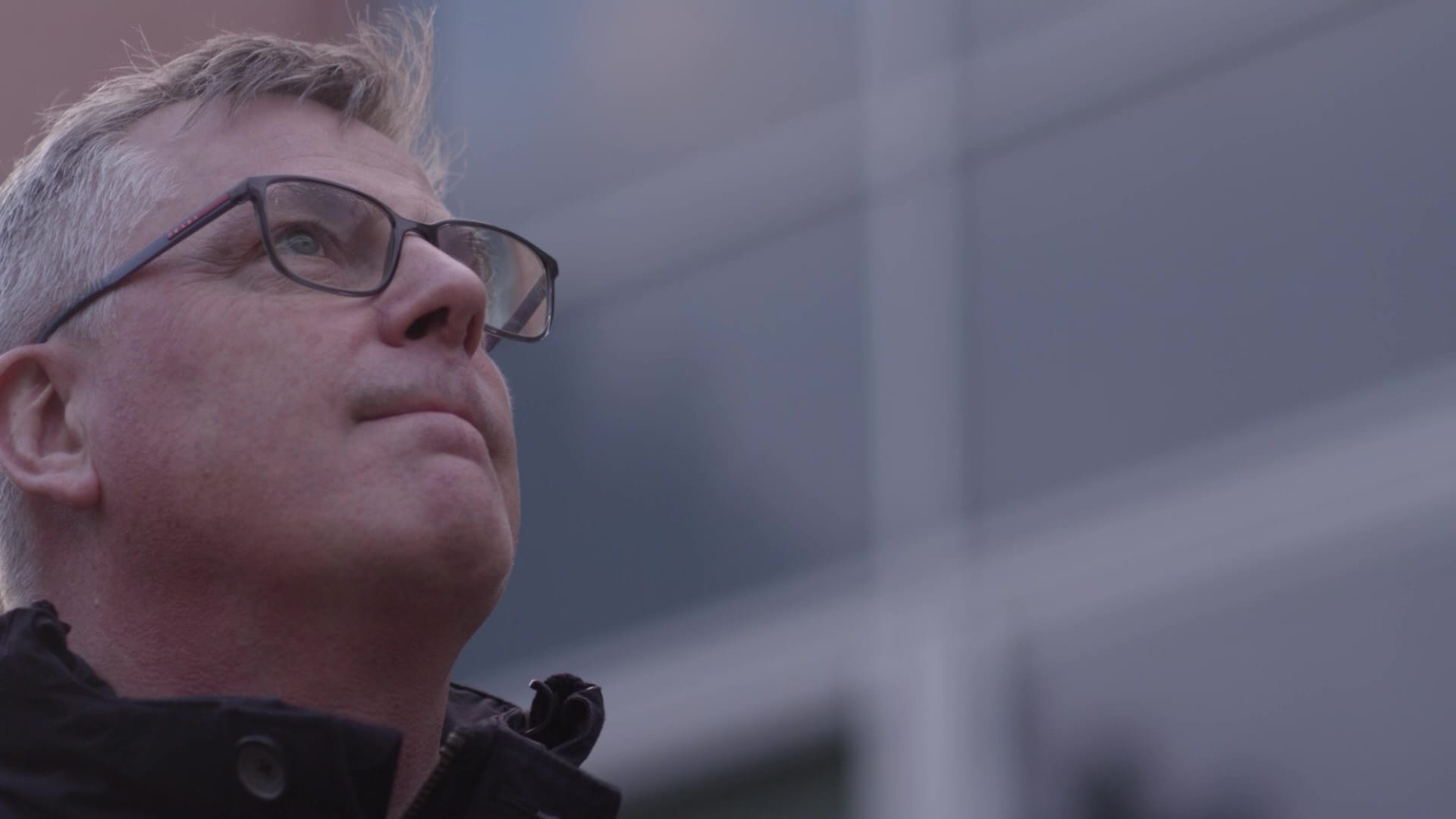 Alumni aux lunettes regardant vers le haut devant une façade vitrée, vidéo institutionnelle ESTP grande école de la construction