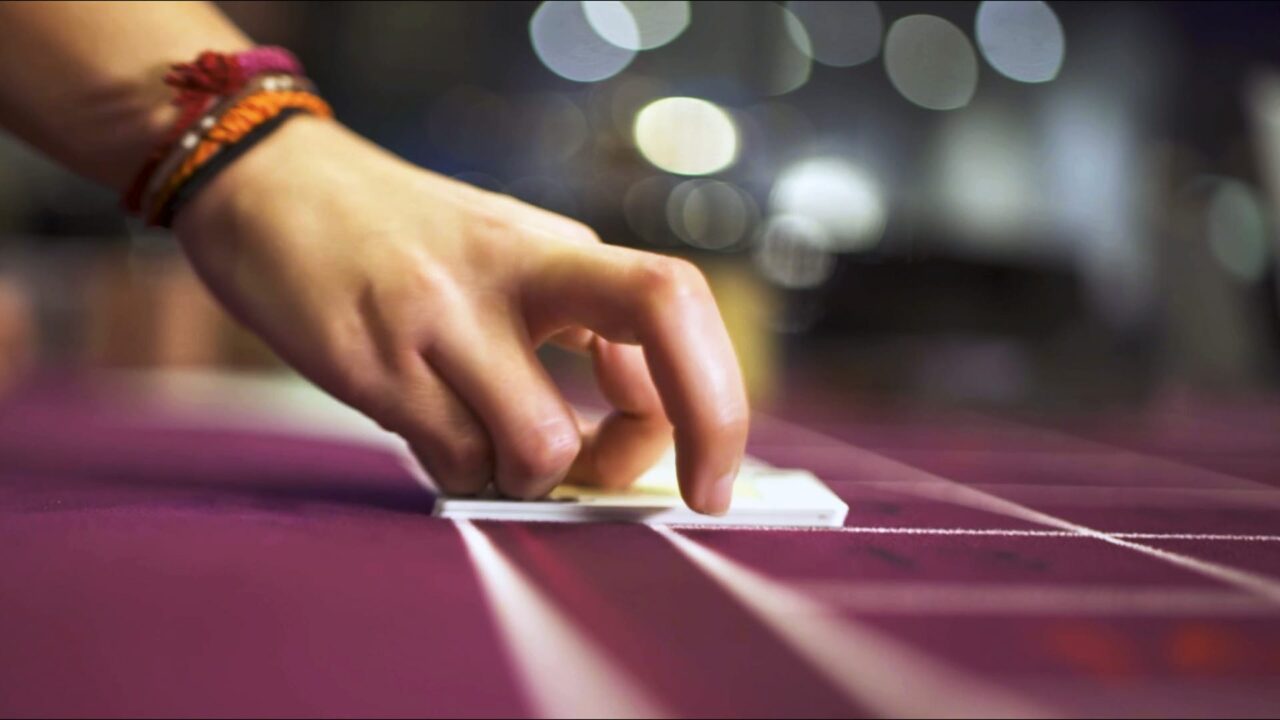 Main saisissant des cartes sur tapis bordeaux, spot TV pour Joa, enseigne de divertissement