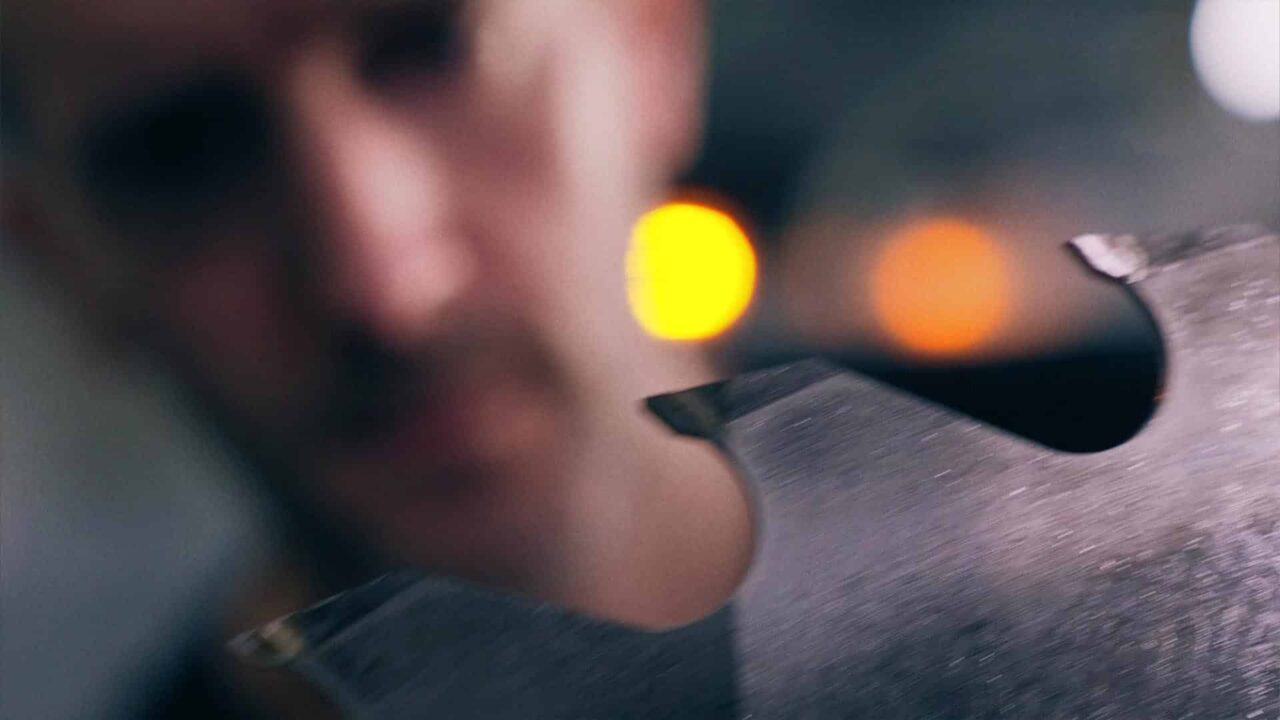Main d'artisan sur pièce métallique, bokeh lumineux, savoir-faire industriel La Forézienne en vidéo institutionnelle