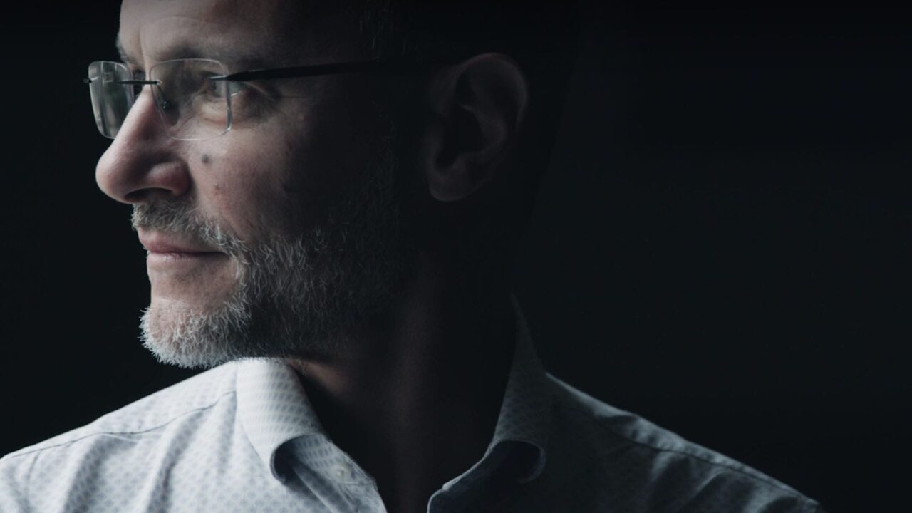 Homme barbu aux lunettes filmé en clair-obscur, film de marque Ecofi, groupe financier à mission