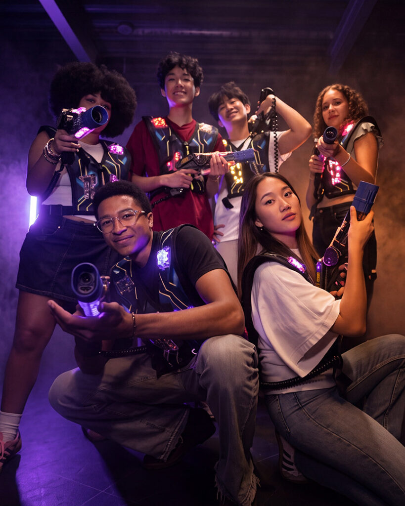 Spot publicitaire Megazone : six joueurs posent avec leurs lasers dans une arène enfumée aux néons violets